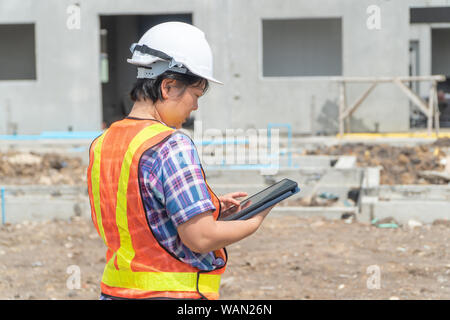 Asiatische Frauen engineering hält einen Tablet-PC für den Einsatz in der Kontrolle von Baustellen für Genauigkeit und in Übereinstimmung mit dem Plan. Konzept der Gleichen Stockfoto