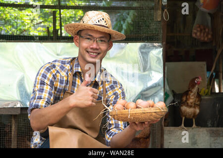 Junge Intelligenter Landwirt wear Plaid Shirt braun Schürze halten Frische Hühnereier in Warenkorb auf einer Hühnerfarm in ihm home Bereich Stockfoto