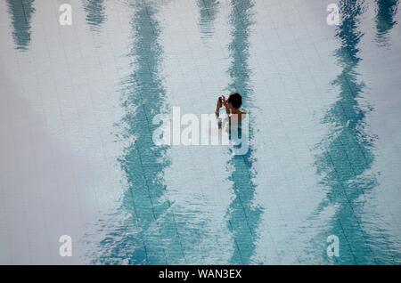 Ein japanischer Tourist können Sie über sein Mobiltelefon in ein Hilton Pool malta Stockfoto