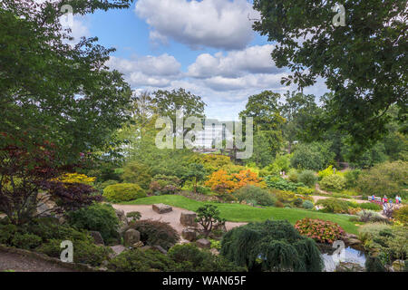 Blick durch die Bäume aus dem Steingarten auf die Glasshouse in RHS Garden, Wisley, Surrey, Südost England im Sommer an einem sonnigen Tag Stockfoto