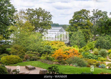 Blick durch die Bäume aus dem Steingarten auf die Glasshouse in RHS Garden, Wisley, Surrey, Südost England im Sommer an einem sonnigen Tag Stockfoto