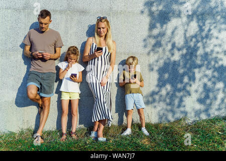 Bild von Eltern und Kindern mit Telefonen in der Hand stehen auf Betonwand auf der Straße im Sommer Tag Stockfoto