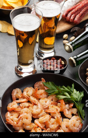 Bier vom Fass und Snacks auf Stein. Muttern, Pommes, Würstchen und Garnelen Stockfoto