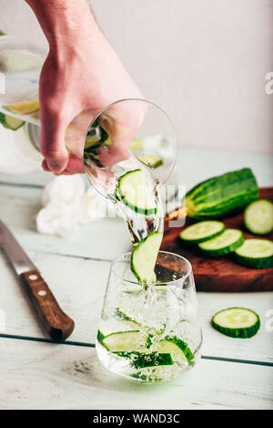 Hand mit Krug gießt detox Wasser mit in Scheiben geschnittenen Gurken Stockfoto