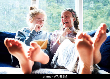 Junge Mädchen sitzen auf einer Couch auf einen Bildschirm schaut und lacht Stockfoto