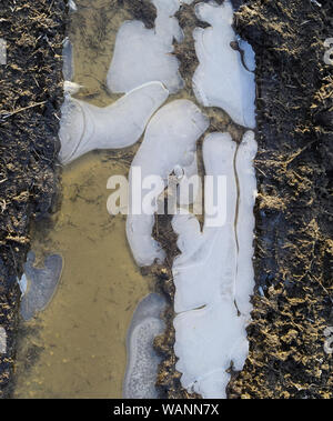 Eis auf einer schlammigen Pfütze auf einer unbefestigten Straße. Stockfoto