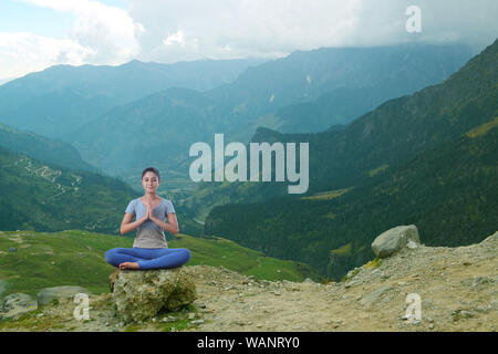 Junge Frau, die Yoga praktiziert, sitzt auf Felsen Stockfoto