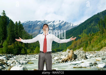 Unbeschwerter Geschäftsmann, der mit ausgestrecktem Arm steht, Beas River, Manali, Himachal Pradesh, Indien Stockfoto