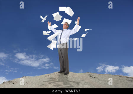Papiere, die auf einen Geschäftsmann fallen, der auf dem Hügel steht Stockfoto