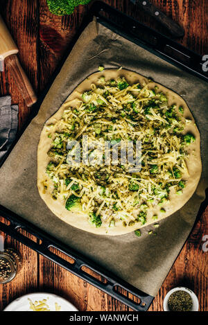 Hausgemachte Pizza mit Brokkoli, Pesto, Gewürze und Käse in ein Backblech bereit für den Backofen. Ansicht von oben Stockfoto