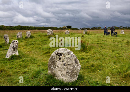 Paar Radfahrer Spaziergang durch Wiese von Standing Stone Circle rief Merry Maidens von Boleigh in Cornwall, England Stockfoto