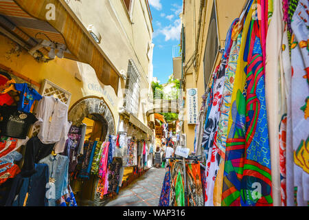 Touristen zu Fuß die engen Pfade mit Kleidung und Souvenirs zwischen den Geschäften in der bunten Resort City von Positano, Italien gesäumt. Stockfoto