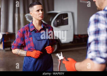 Weibliche automechanic in der Uniform hört ihr Mentor, wie er erklärt ihr, was sie zu tun haben. Stockfoto