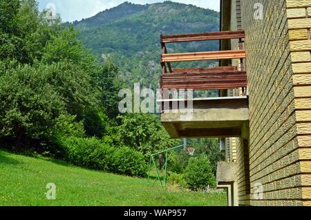 Ein Balkon aus Holz von einem gelben Backstein Bergdorf Haus mit einem Basketball outdoor Court und ein Berg im Hintergrund, einem Wald auf der linken Seite Stockfoto