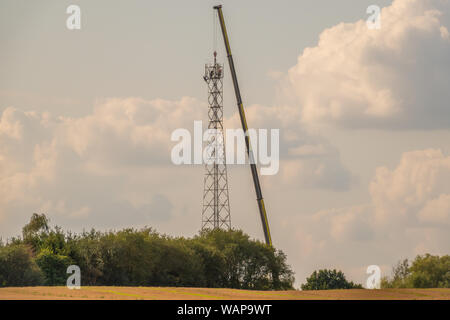 Eine 5-G-Sendemast errichtet auf einem Feld mit der Hilfe von einem riesigen Kran Stockfoto