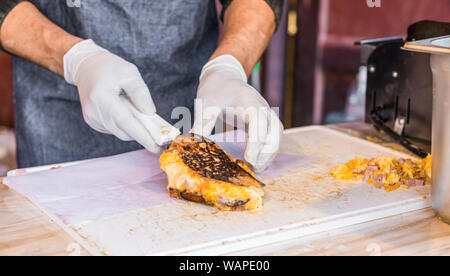 Chef an einer Straße Markt vorbereiten Sandwich mit gegrilltem geschmolzenem Käse und Speck Stockfoto