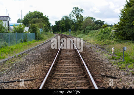 Ein einziger Satz von Bahngleisen führt zu einem Fluchtpunkt am Horizont, die Bahnlinie schneidet durch ländliche britische Landschaft Stockfoto