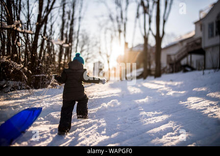 Junge weg in den Sonnenuntergang ziehen blau Schlitten hinter ihm, auf einem Hügel Stockfoto