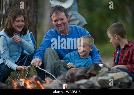 Glückliche Familie sitzt um ein Lagerfeuer und toasten Marshmallows in den Wald. Stockfoto