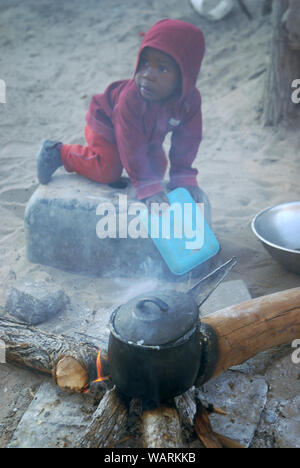 Junge helfen einen Topf Nshima, einem dicken Brei aus fein gemahlenen Maismehl, Mwandi, Sambia, Afrika zu kochen. Stockfoto