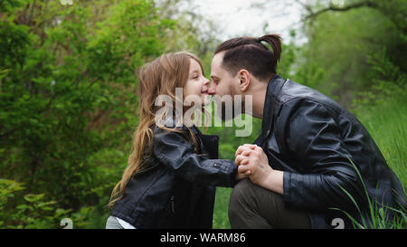 Modernes, stilvolles Familie Fuß in den Park. Tochter Küsse und Umarmungen Vati. Zeit zusammen. Familie suchen. Urban casual Outfit. Stockfoto