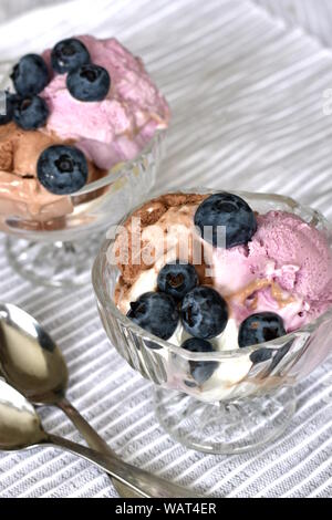 Zwei Glasschalen mit Rosa und braun Eis mit Blaubeeren, auf weiß gestreifter glänzender Oberfläche serviert dekoriert. Vertikale. Stockfoto