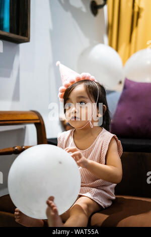 Asiatische kleinkind Mädchen feiert Geburtstag und trägt einen rosa Hut und halten ein Ballon. Stockfoto