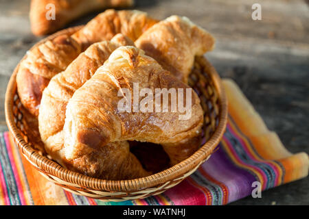 Warme Croissants, in einem Korb mit einem gestreiften Serviette serviert serviert, über alten Holztisch. Retro Stil Verarbeitung und Vignette Stockfoto