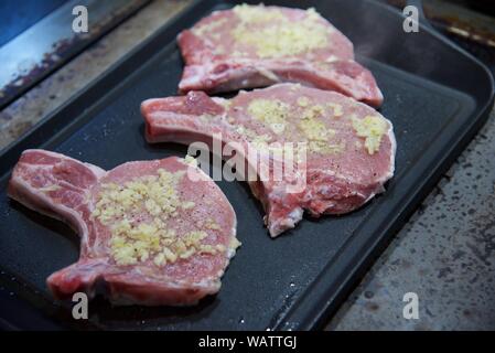 Schweinekoteletts: Schweinekoteletts mit zerdrückten Knoblauch, Salz und gemahlener schwarzer Pfeffer start Kochen auf einem Aluminium Griddleplatte gekleidet Stockfoto