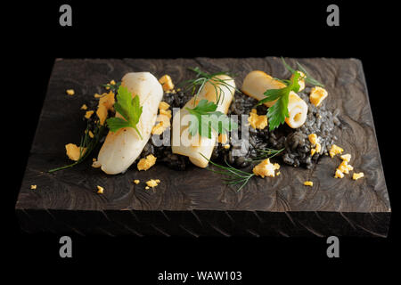 Schwarz isotto mit Tintenfisch und gebratene calamary auf Holzbrett, isoliert auf Schwarz Stockfoto