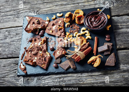 Schokolade mit getrockneten Feigen und Cashew füllen sich auf Stücke auf einem schwarzen Stein Fach mit Zutaten gebrochen, horizontale Ansicht von oben, close-up Stockfoto