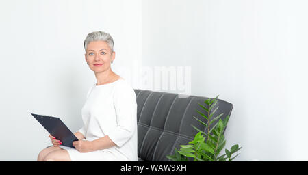 Reife Frau sitzt in einem Büro schreibt in einem Fragebogen oder liest finanzielle Dokumente. Stockfoto