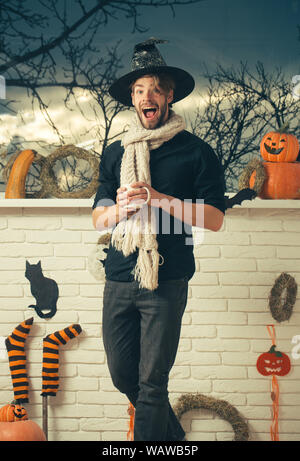 Halloween macho mit offenen Mund tragen Hexe Hut und Schal. Mann hält Schale am Fenster mit Bäume im Herbst. Zaubertrank Konzept. Urlaub Symbole und de Stockfoto