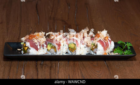 Spezielle Uramaki mit Thunfisch, rohe Garnelen, Omelette, Käse Sauce, Zwiebeln, Tabasco, Kaviar und Katsuobushi, dunkles Holz Tisch Hintergrund Stockfoto