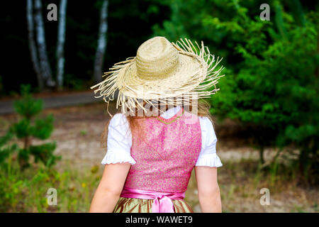 Rückseite der jungen Frau in Dirndl und Strohhut Wandern im Wald Stockfoto