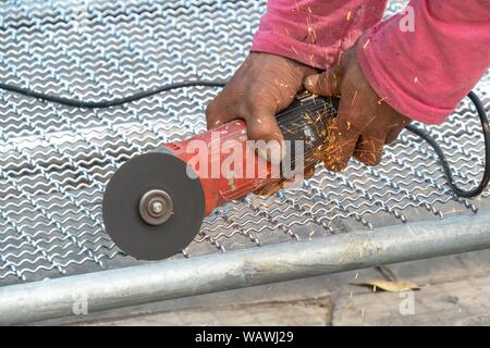 Man Winkelschleifer ohne Schutzabdeckung Schneiden von Metall net Vogelkäfig zu machen. Stockfoto