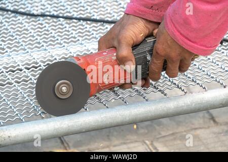 Man Winkelschleifer ohne Schutzabdeckung Schneiden von Metall net Vogelkäfig zu machen. Stockfoto