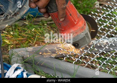 Man Winkelschleifer ohne Schutzabdeckung Schneiden von Metall net Vogelkäfig zu machen. Stockfoto