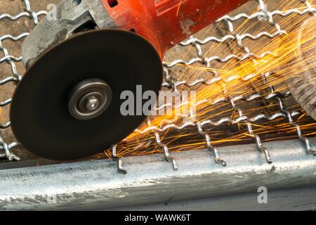 Man Winkelschleifer ohne Schutzabdeckung Schneiden von Metall net Vogelkäfig zu machen. Stockfoto