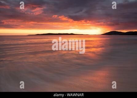 Wellen auf einem Sandstrand, dramatischer Sonnenuntergang mit bewölktem Himmel über den Atlantik, die Insel Harris, Schottland, Vereinigtes Königreich Stockfoto