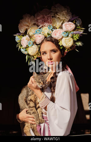 Brünette Mädchen in einem weißen ukrainischen authentische nationale Kostüm und ein Kranz aus Blumen posiert für die Kamera. Close-up. Stockfoto