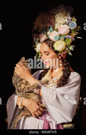 Brünette Mädchen in einem weißen ukrainischen authentische nationale Kostüm und ein Kranz aus Blumen posiert für die Kamera. Close-up. Stockfoto