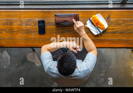 Junge asiatischer Mann Tippen auf Tablet Bildschirm im rustikalen Wirtsstube Stockfoto