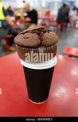 Chocolate muffin auf braun Kaffee Tasse auf dem roten Tisch mit unscharfen Leute im Hintergrund Stockfoto