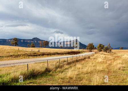 Leere Landstraße durch Bergwiesen in der capertee Valley, NSW, Australien schneiden, mit Sandstein Bergrücken und natürlichen Buschland im Hintergrund Stockfoto