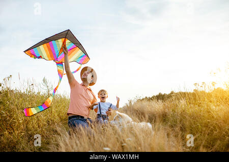 Portrait eines glücklichen Vater und Sohn Holding farbenfrohe, Drachen, während sitzen zusammen auf dem Feld bei Sonnenuntergang Stockfoto