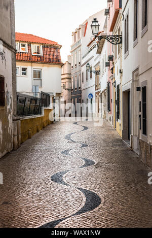 Verwinkelten engen, kopfsteingepflasterten Gasse in Portugiesisch Pflaster calçada Muster entfernt zwischen traditionellen weißen und bunten Häusern aus Stein Stockfoto