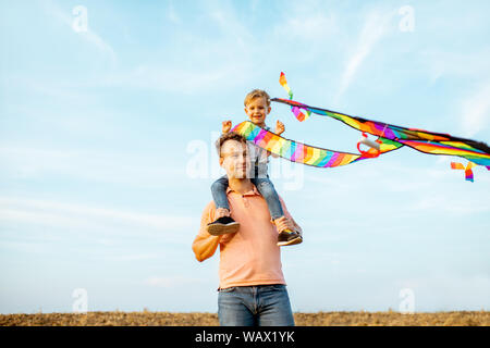 Portrait eines glücklichen Vater und Sohn auf den Schultern mit farbenfrohen, Kite auf dem Hintergrund des blauen Himmels. Konzept einer glücklichen Familie und Sommer Acti Stockfoto