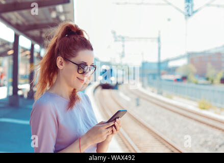 Junge Frau mit Ihrem Handy auf u-Plattform, Kontrolle Nachricht sms-e-mail oder mit der Bahn planen. Mädchen von SMS-Nachrichten auf dem Smartphone während Stadt Zug approa Stockfoto