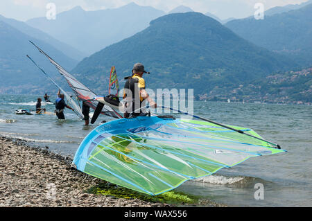 Comer see, Italien - Juli 21., 2019. Mann Windsurfer mit einem Segel in der Bergsee, Surf Board im Vordergrund. Alp Berge auf einem Hintergrund Stockfoto